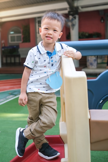 Pełnej długości portret uśmiechniętego azjatyckiego 3-4-letniego chłopca pozuje do kamery podczas zabawy na drabince na placu zabaw