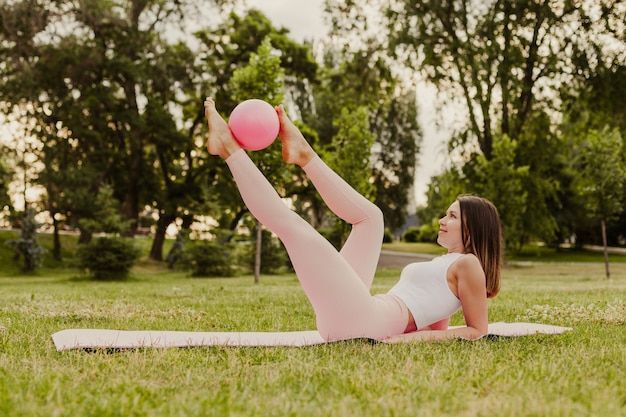 Pełnej długości szczupła kobieta w różowej górnej pozie z piłką pilates, koncepcja pielęgnacji ciała i zdrowia.