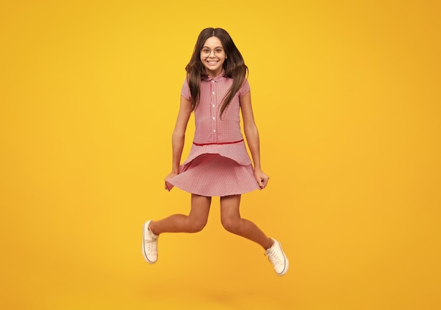 Pełnej długości wesoły nastolatek dzieciak skacze cieszyć się radością wygraną na żółtym tle Mała dziewczynka w letniej sukience skacze