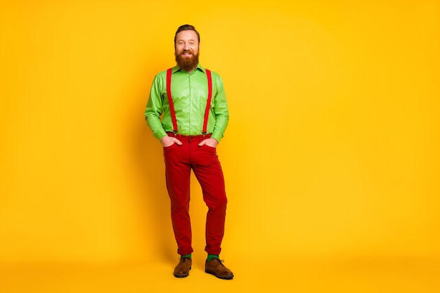 Pełnej długości zdjęcie atrakcyjnego macho zabawny facet dobry nastrój wesoły ząb uśmiechnięty nosić zieloną koszulę czerwone szelki spodnie skarpetki obuwie izolowany połysk kolor
