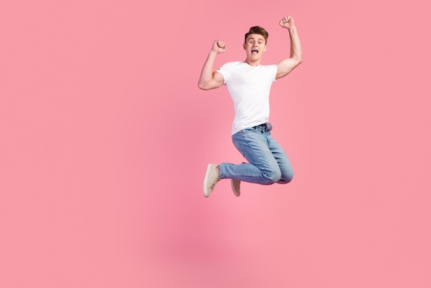 Pełnej długości zdjęcie atrakcyjnego szalonego faceta skacze wysoko, wspierając cel drużyny piłkarskiej na białym tle pastelowego koloru tła