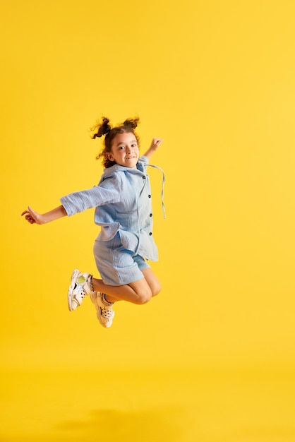Pełnometrażowy portret aktywnego małego dziecka dziewczynka w przypadkowych ubraniach radośnie skacze przeciw