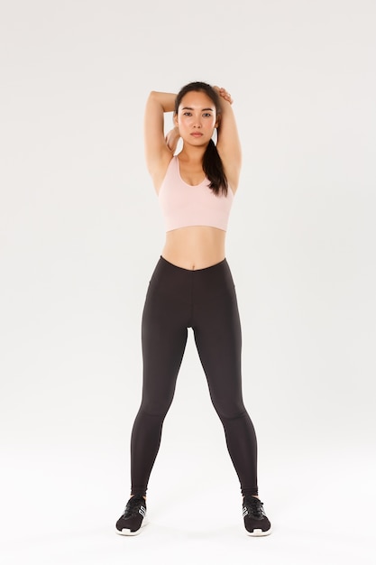 Pełnowymiarowa skupiona i zmotywowana azjatycka athelte, brunetka fitness wyglądająca na zdeterminowaną podczas wykonywania ćwiczeń rozciągających, rozgrzewka przed treningiem, trzymanie się za ręce.
