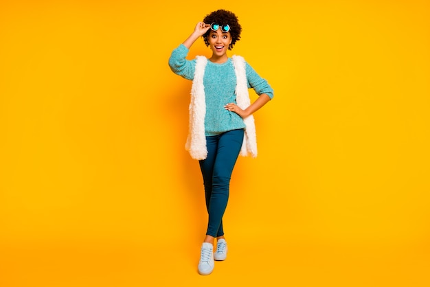 Pełnowymiarowe zdjęcie funky szalonej afroamerykanki dotknąć okulary przeciwsłoneczne usłyszeć jesień sprzedaż w czarny piątek pod wrażeniem krzyk nosić białe stylowe modne kamizelki niebieskie spodnie buty izolowane połysk kolor tło