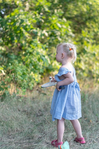 Pełnowymiarowy portret dziecka w niebieskiej sukience z rakietą w dłoniach Mała dziewczynka gra w badmintona poza ramą pionową
