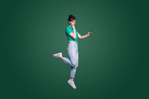 Pełny długość portret rozważna wątpliwa kobieta opowiada na telefonie komórkowym odizolowywającym nad zielonym tłem