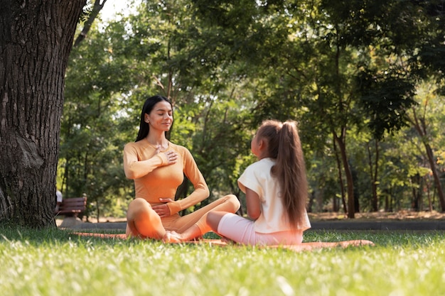 Zdjęcie pełny strzał kobiety i dziewczyny medytujących w parku