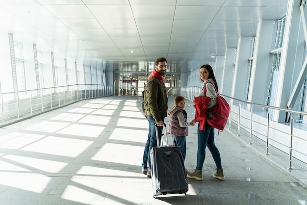 Pełny widok szczęśliwej rodziny matki, ojca i córki idących z walizkami do hali odlotów Koncepcja podróży i podróży