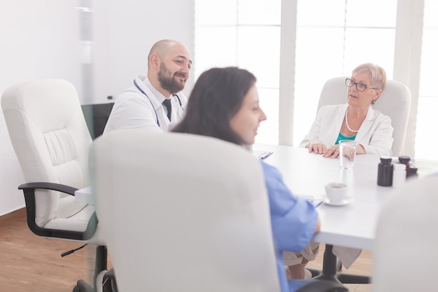 Personel medyczny uśmiechający się w sali konferencyjnej podczas rozmowy z innym lekarzem w białym fartuchu. Terapeuta kliniczny z kolegami rozmawiającymi o chorobie, ekspert, specjalista, komunikacja.