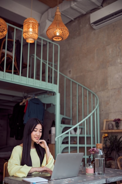 Pewna Azjatycka kobieta biznesu w żółtym swetrze podczas pracy z myślą o chwili na laptopie w kawiarni
