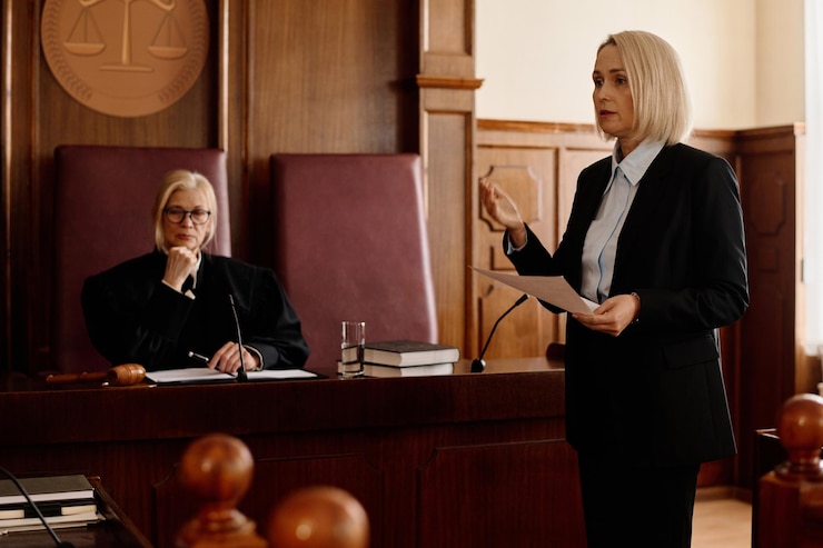 Zdjęcie pewna, blond prokuratorka z dokumentem prawnym patrzy na podejrzanego i jego adwokata.