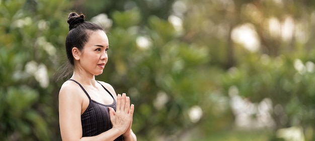 Pewna kobieta w średnim wieku Azjatka w stroju sportowym robi ćwiczenia jogi na macie do jogi na świeżym powietrzu rano na podwórku. Młoda kobieta robi ćwiczenia jogi na świeżym powietrzu w publicznym parku przyrody