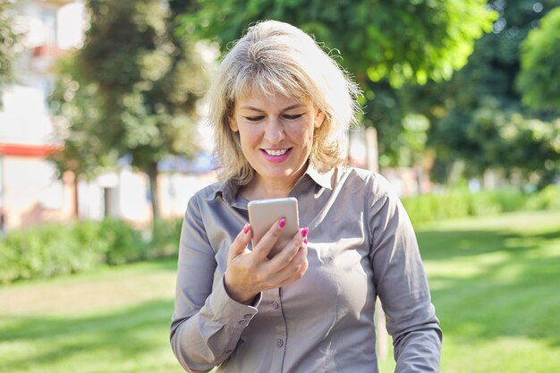 Pewna siebie biznesowa kobieta w średnim wieku ze smartfonem, portret udanej kobiety w mieście