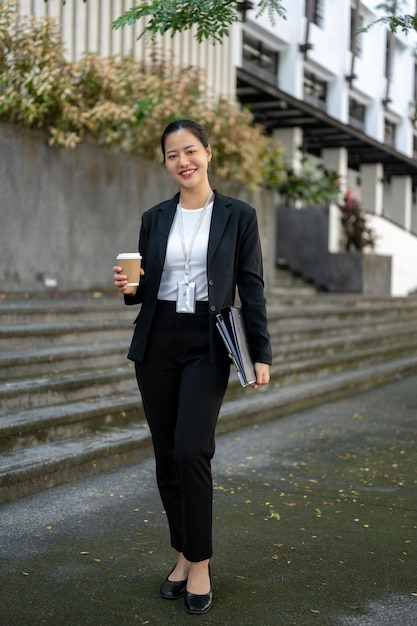Pewna siebie i atrakcyjna, tysiącletnia azjatycka bizneswoman stoi na zewnątrz budynku