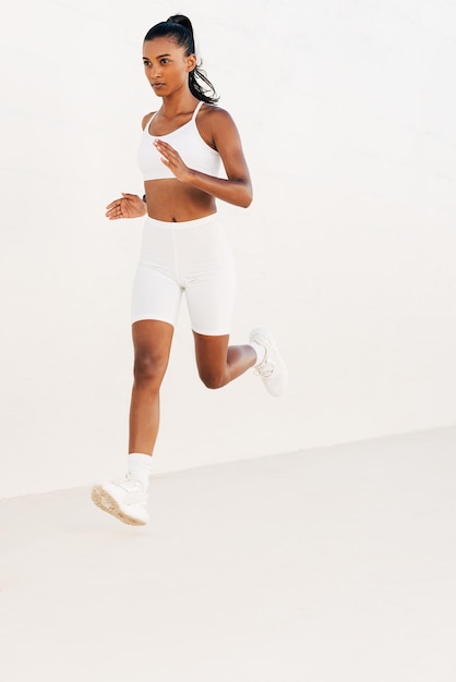 Pewna siebie kobieta biegnie sprintem po białej ścianie Szczupły biegacz w białym stroju fitness biegający na zewnątrzx9xA