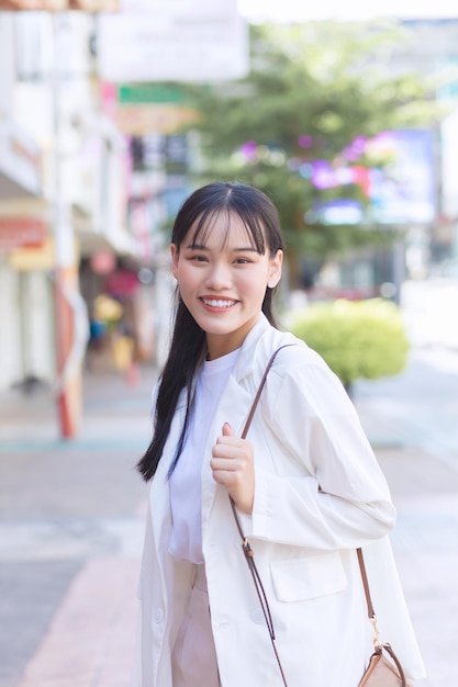 Pewna siebie młoda Azjatka, która nosi białą koszulę, torebka na ramię uśmiecha się radośnie podczas chodzenia