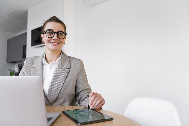 Pewna siebie profesjonalna kobieta w eleganckiej kurtce uśmiecha się podczas pracy na cyfrowym tabletie siedzącym