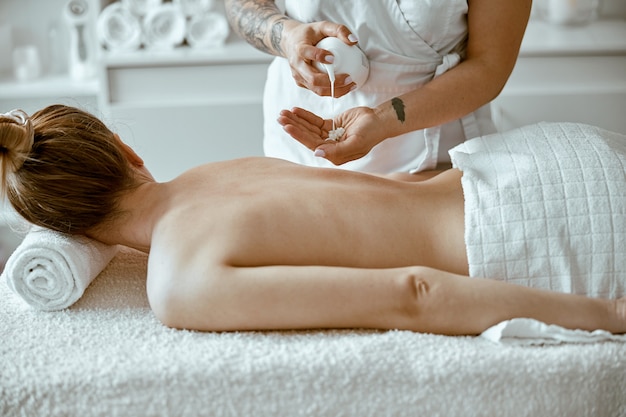 Pewna siebie specjalistka wykonuje relaksujący masaż ciała dla pięknej szczupłej kaukaskiej damy w minimalistycznym salonie spa