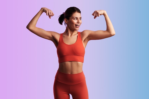 Pewna siebie, szczęśliwa sportowczyna pokazująca biceps w studiu.