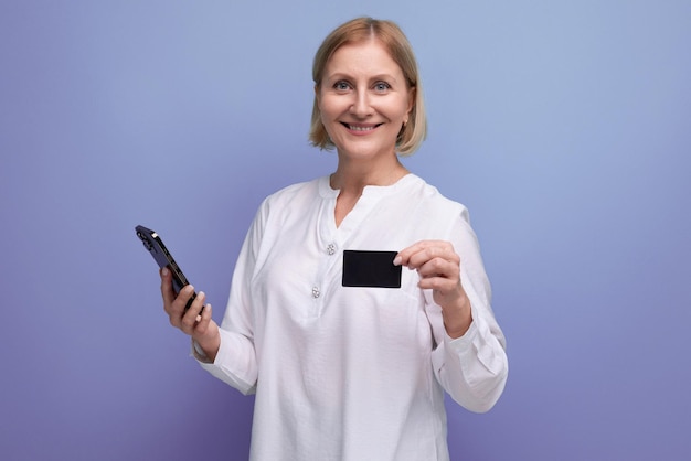 Pewna siebie szczupła blondynka dojrzała kobieta w białej bluzce trzymająca plastikową kartę na zakupy z makietą