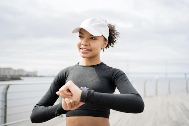 Pewna siebie, wysportowana kobieta używa urządzenia śledzącego na swoim smartwatchu do treningu sportowego w odzieży sportowej