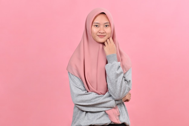 Pewność siebie młodej Azjatki zaczyna się od uśmiechu noszącego swobodny hidżab, odizolowany na różowym tle