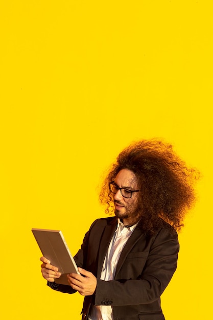 Pewny siebie biznesmen trzymający cyfrową tabletkę i uśmiechniętą pozycję na żółtym tle