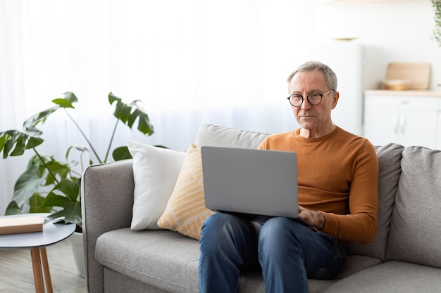 Pewny siebie, dorywczo dojrzały mężczyzna, używający laptopa w domu