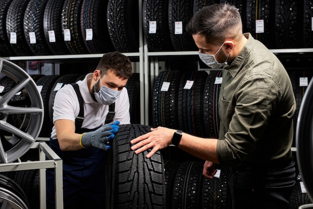 Pewny Siebie Mechanik W Masce I Klient Sprawdzający Opony W Sklepie, Prowadzący Rozmowę W Sklepie, Klient Zamierza Dokonać Zakupu