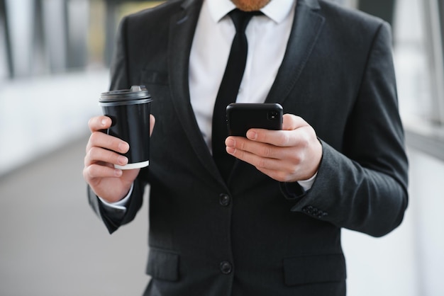 Pewny siebie młody biznesmen używający telefonu komórkowego i pijący kawę w mieście