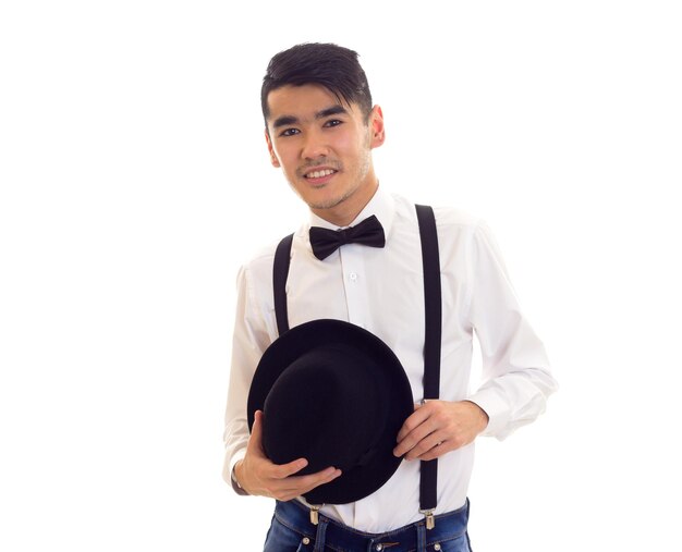Pewny siebie młody człowiek w białej koszuli z czarnymi szelkami w muszce i kapeluszu w studio