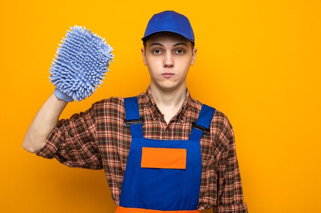 Pewny siebie młody sprzątacz ubrany w mundur i czapkę trzymającą szmatę