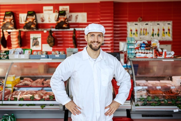 Pewny siebie rzeźnik stoi w mięsnym domu i uśmiecha się do kamery