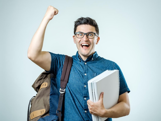 Pewny siebie student Portret studyjny przystojnego młodego mężczyzny z plecakiem Odizolowany na szaro