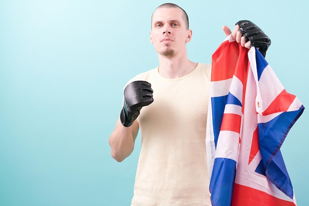 Pewny siebie zawodnik MMA w czarnych rękawiczkach trzyma flagę Wielkiej Brytanii gotową do walki na niebieskim tle Pozycja bojowa Poza nokaut Łysy Mieszane sztuki walki Uderz Ciężki Mocne uderzenie Wygraj gol