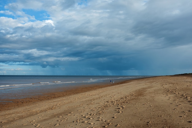 Piaszczysta plaża, morze i zachmurzone błękitne niebo w Anglii w dzień