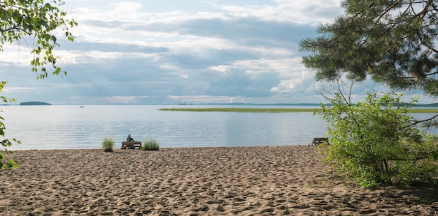 Piaszczysta plaża na brzegu rozległego jeziora kobieta turystka siedzi na ławce wykonanej ze starych palet