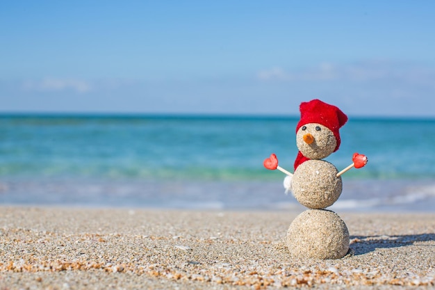 Zdjęcie piaszczysty bałwan w czerwonym kapeluszu santa opalając się w salonie na plaży.