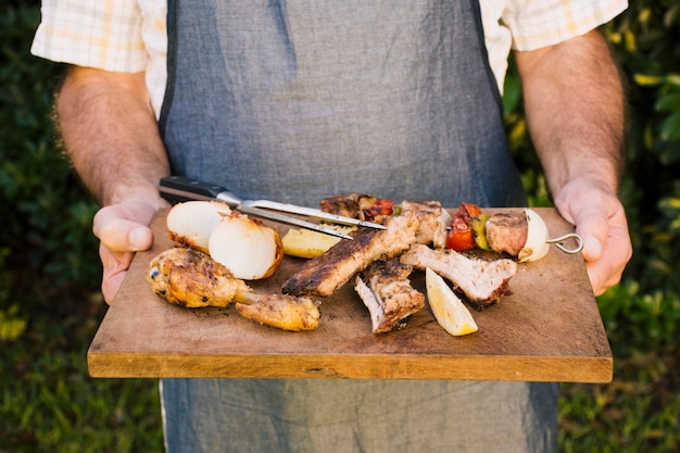 Piec na grillu soczysty mięso i warzywa na drewnianym biurku w rękach