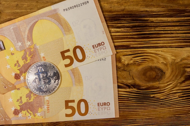 Pięćdziesiąt banknotów euro i srebrny bitcoin na drewnianym tle Widok z góry