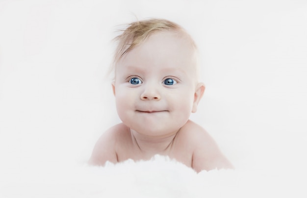 Zdjęcie pięciomiesięczny blond chłopiec o niebieskich oczach leży na brzuchu, uśmiechając się słodko,