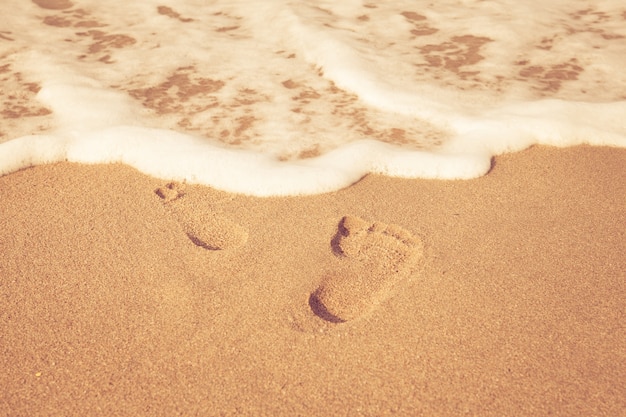 pieczęć stóp na piasku na plaży z sunshine rano, zabytkowe stylu koloru