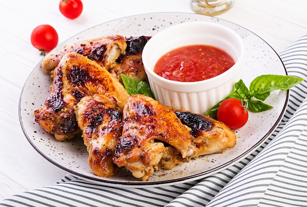 Pieczone skrzydełka z kurczaka w stylu azjatyckim i sosem pomidorowym na talerzu.