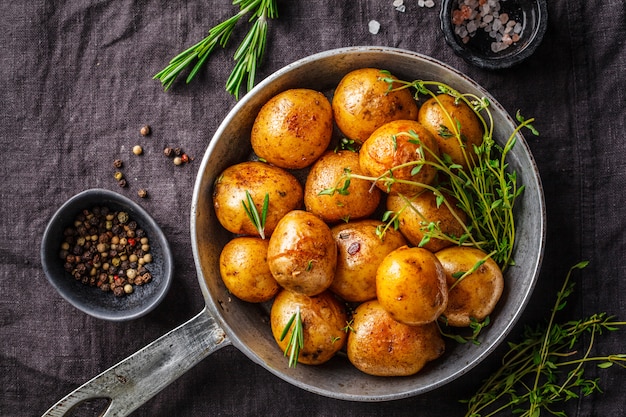 Pieczone ziemniaki na patelni żeliwnej, ciemne tło.