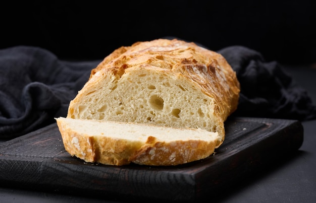 Pieczony cały owalny chleb z białej mąki pszennej na czarnym stole, świeże wypieki