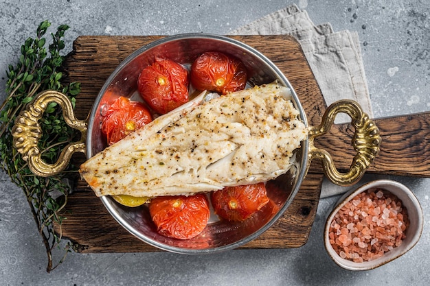 Zdjęcie pieczony filet rybny z łupacza na patelni z pomidorami i ziemniakami szare tło widok z góry