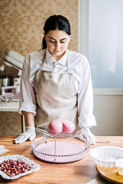 Piekarz robi idealne niestandardowe różowe ciasto w kształcie serca w piekarni kuchennej na zamówienie w internetowym sklepie z ciastami