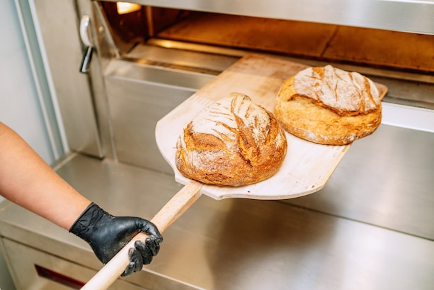 Piekarz wkłada chleb do pieca piekarniczego kuląc się na podłodze piekarni