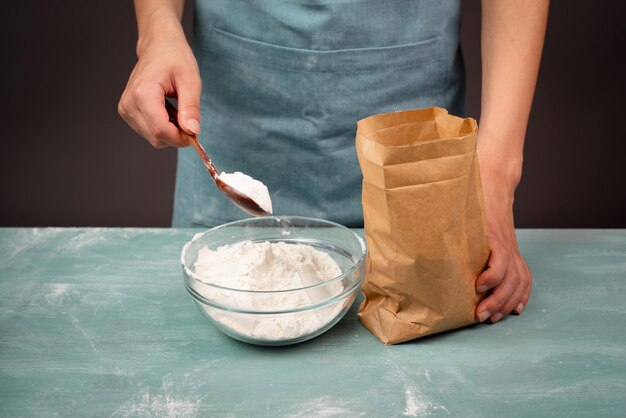 Piekarz wkłada mąkę łyżką do papierowej torby miski ze składnikiem do pieczenia chleba, pizzy lub ciasta