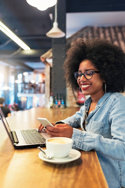 Piękna Afro Amerykańska Kobieta Za Pomocą Telefonu Komórkowego I Laptopa W Kawiarni. Koncepcja Komunikacji.